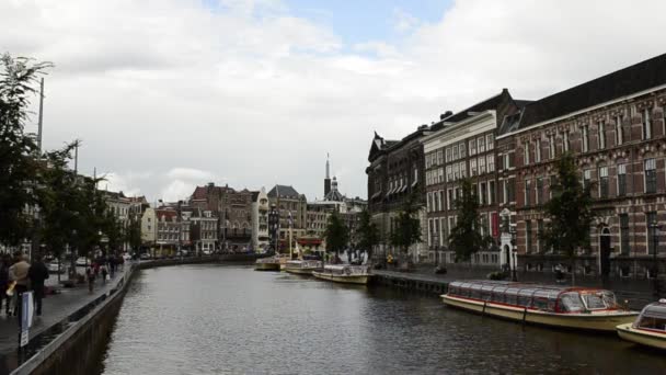 アムステルダム オランダ 2019 典型的な家に囲まれた旧市街の魅力的な運河 人々は運河 係留観光船に沿って歩く 暗い雲と灰色の日 静的なフレーム — ストック動画