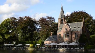 Bruges, Belçika - Ağustos 2019: Aşk Gölü olarak da bilinen büyüleyici Minnewater: restoran olarak kullanılan şato suya yansıyor. Ağaçlar yeşil bir çerçeve.