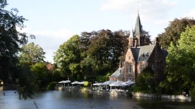 Bruges, Belçika - Ağustos 2019: Aşk Gölü olarak da bilinen büyüleyici Minnewater: restoran olarak kullanılan şato suya yansıyor. Ağaçlar yeşil bir çerçeve.