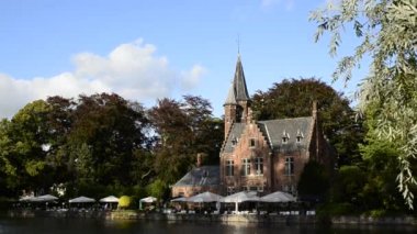 Bruges, Belçika - Ağustos 2019: Aşk Gölü olarak da bilinen büyüleyici Minnewater: restoran olarak kullanılan şato suya yansıyor. Ağaçlar yeşil bir çerçeve.