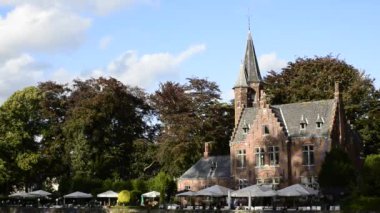Bruges, Belçika - Ağustos 2019: Aşk Gölü olarak da bilinen büyüleyici Minnewater: restoran olarak kullanılan şato suya yansıyor. Ağaçlar yeşil bir çerçeve.