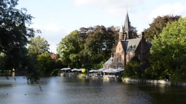 Bruges, Belçika - Ağustos 2019: Aşk Gölü olarak da bilinen büyüleyici Minnewater: restoran olarak kullanılan şato suya yansıyor. Ağaçlar yeşil bir çerçeve.
