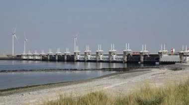 Oosterscheldekering, Hollanda - Ağustos 2019: Çok modern anti-fırtına barajı manzarası: Zorlayıcı mühendislik çalışmalarının arka planında, rüzgar türbinleri rüzgar enerjisinden faydalanıyor.
