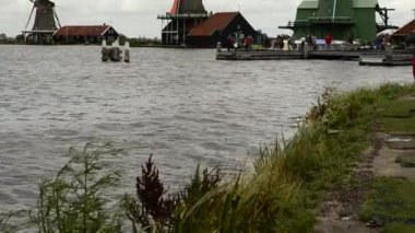 Zaanse Schans, Hollanda - Ağustos 2019: Kuzeydoğu Amsterdam Zaan Nehri üzerinde yer alan küçük bir topluluktur. Nehir kıyısındaki değirmenlerin manzarası parlak renkleriyle göze çarpıyor. Bulutlu bir gün.