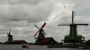 Zaanse Schans, Hollanda - Ağustos 2019: Kuzeydoğu Amsterdam Zaan Nehri üzerinde yer alan küçük bir topluluktur. Nehir kıyısındaki değirmenlerin manzarası parlak renkleriyle göze çarpıyor. Bulutlu bir gün.