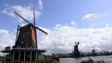 Zaanse Schans, Hollanda - Ağustos 2019: Kuzeydoğu Amsterdam Zaan Nehri üzerinde yer alan küçük bir topluluktur. Nehir kıyısındaki değirmenlerin manzarası parlak renkleriyle göze çarpıyor. Bulutlu bir gün.
