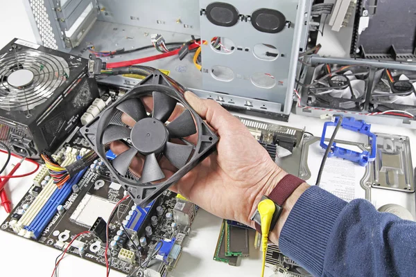 Computer repair  - Computer technician holding dismantled fan during repair process against background of computer parts