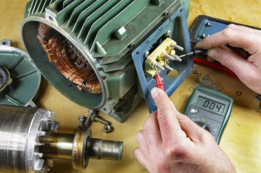 Üç fazlı endüksiyon motor taşıyan onarmak bir tesisatçı/teknisyen motor sargıları direnç okuma bir multimetre ile kontrol.