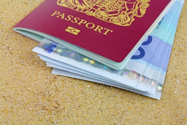 Passports and money  - UK biometric passports with euro notes laying on sand.