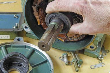 Three phase induction   motor bearing repair  A fitter/technician  checking motor windings resistance readings with a multimeter and  checking for faults on shaft bearings, . clipart