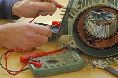 Three phase induction   motor bearing repair  A fitter/technician  checking motor windings resistance readings with a multimeter. clipart