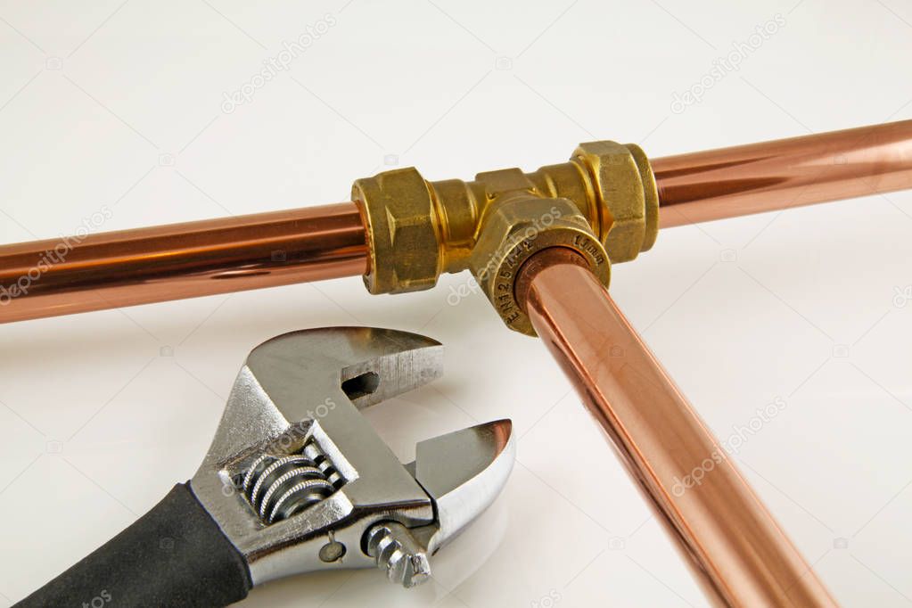 New copper pipework ready for construction  Adjustable wrench, 15mm copper piping and brass joints laid together against a grey background