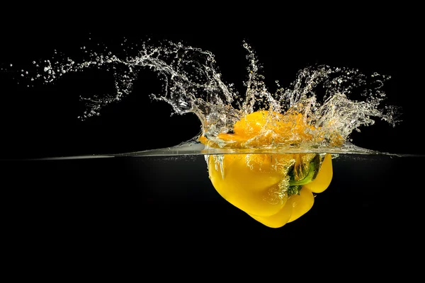 Yellow bell pepper falling in water on black — Stock Photo, Image
