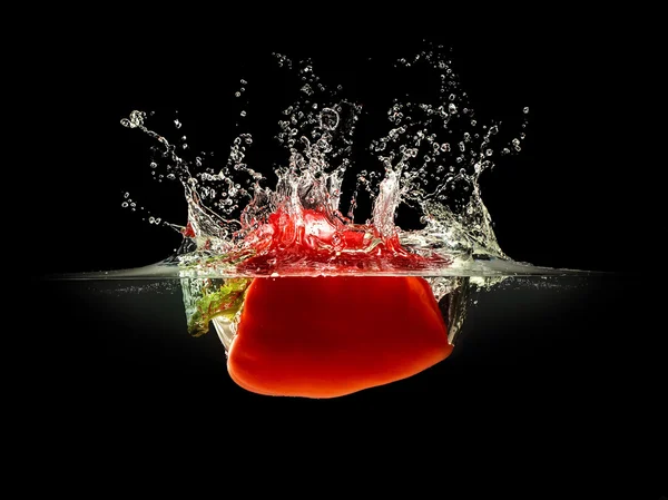 Rote Paprika fällt in Wasser mit Spritzer auf schwarzem Hintergrund — Stockfoto