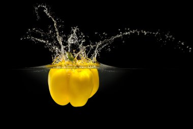 Su sıçrama ile siyah arka plan üzerine düşen sarı dolmalık biber