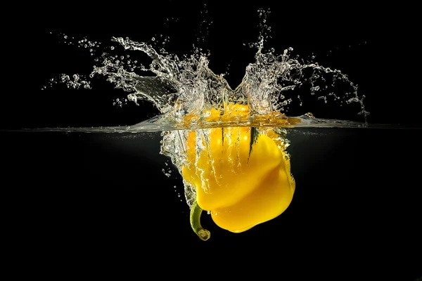 Pimenta amarela caindo na água com respingo no fundo preto — Fotografia de Stock