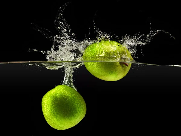 Grupo de manzanas verdes cayendo en el agua sobre negro — Foto de Stock