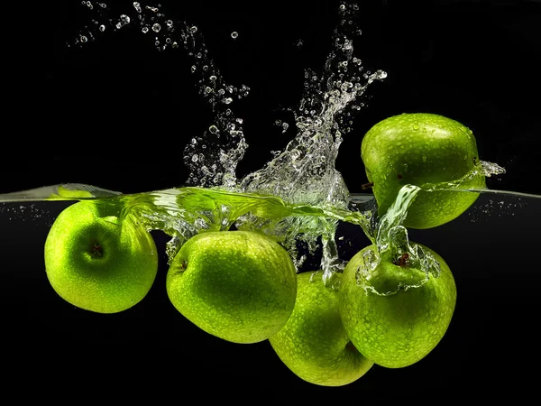 Grupp av gröna äpplen faller i vattnet på svart — Stockfoto