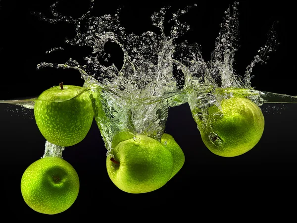 Grupo de manzanas verdes cayendo en el agua sobre negro — Foto de Stock