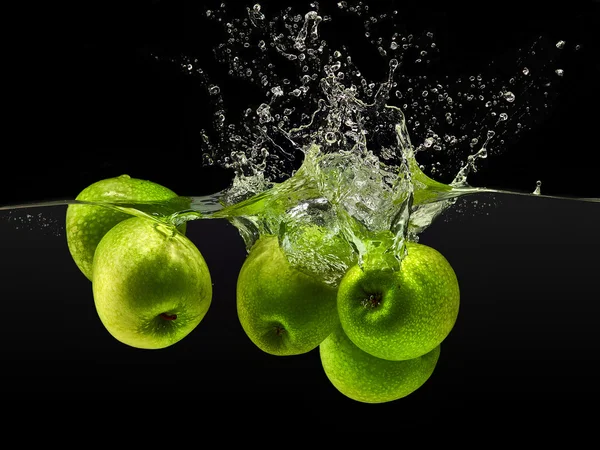 Grupo de maçãs verdes caindo na água sobre fundo preto — Fotografia de Stock