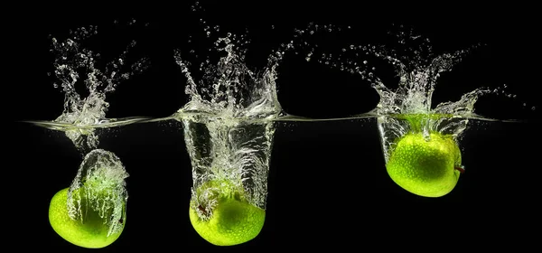 Grönt äpple som faller i vattnet på svart bakgrund — Stockfoto