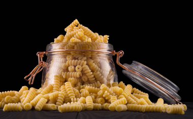 Bir kavanoz fusilli makarna ahşap masa üzerinde izole edilmiş siyah arkaplan