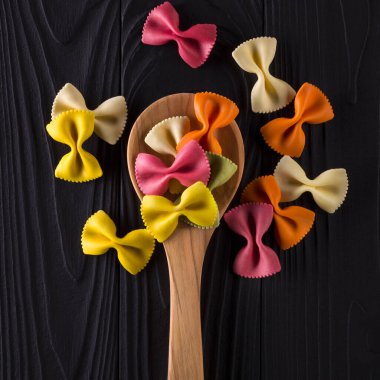 Top view of colorful farfalle pasta on black wooden table with spoon