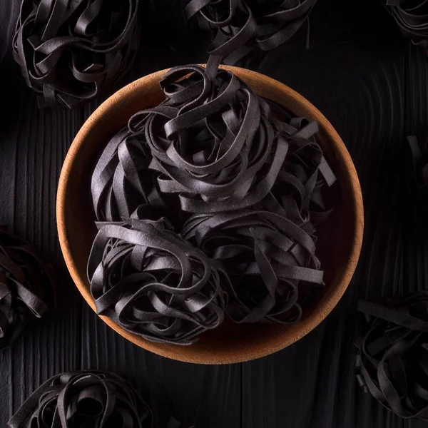 Top view of tagliatelle pasta nests in bowl and scattered on black wooden table — ストック写真