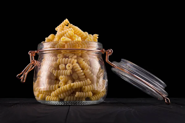 Frasco de massa fusilli sobre mesa de madeira isolada sobre fundo preto — Fotografia de Stock