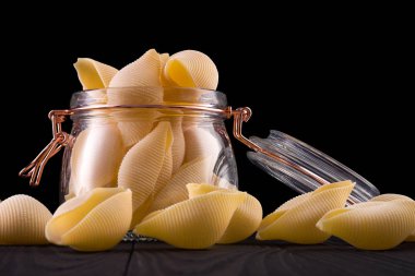 Siyah arka planda izole edilmiş ahşap masa üzerinde koni makarna kavanozu