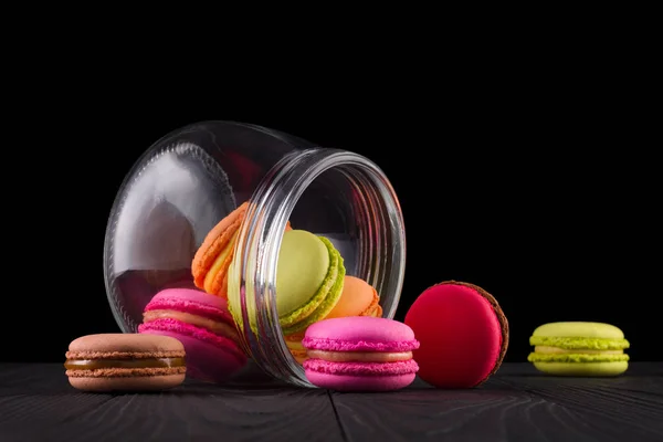 Jar of french colorful macaroon or macaron on wooden table isolated on black