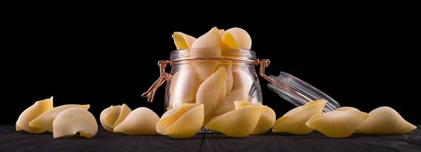 Frasco de conchiglie pasta shell sobre mesa de madeira isolada sobre fundo preto — Fotografia de Stock