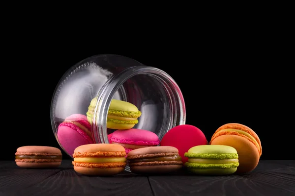 Frasco de macaroons coloridos franceses e montão na mesa de madeira isolada em preto — Fotografia de Stock