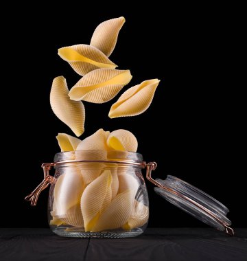 Siyah arka planda izole edilmiş ahşap masa üzerinde koni makarna kavanozu