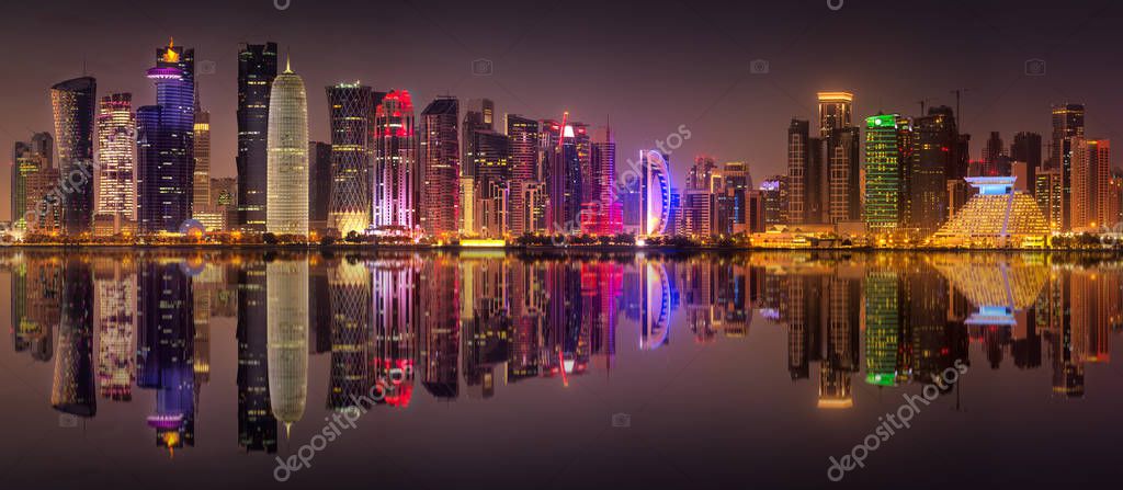 View of park and building in Doha City Center with reflection of buildings on water at night, Qatar