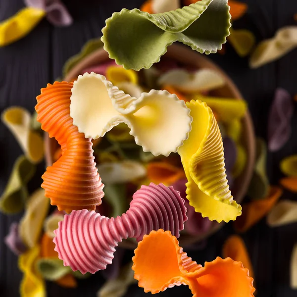Draufsicht auf bunte Farfalle Pasta gebläut und verstreut auf schwarzem Holztisch — Stockfoto
