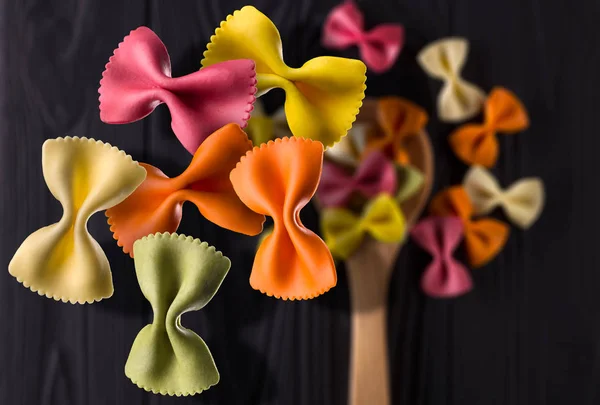 Draufsicht auf bunte Farfalle Pasta gebläut und verstreut auf schwarzem Holztisch — Stockfoto