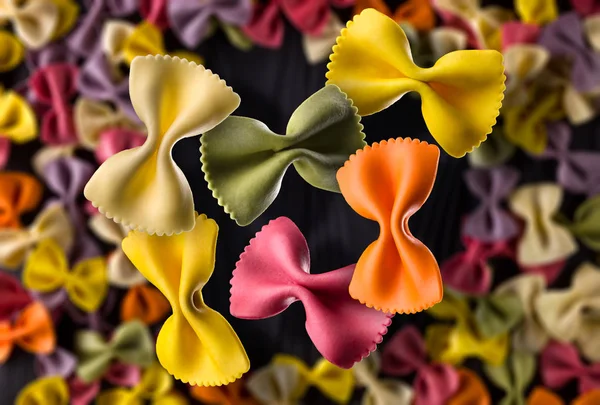 Draufsicht auf bunte Farfalle Pasta gebläut und verstreut auf schwarzem Holztisch — Stockfoto