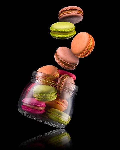 Flying french colorful macaroons and jar on wooden table isolated on black — Stock Photo, Image