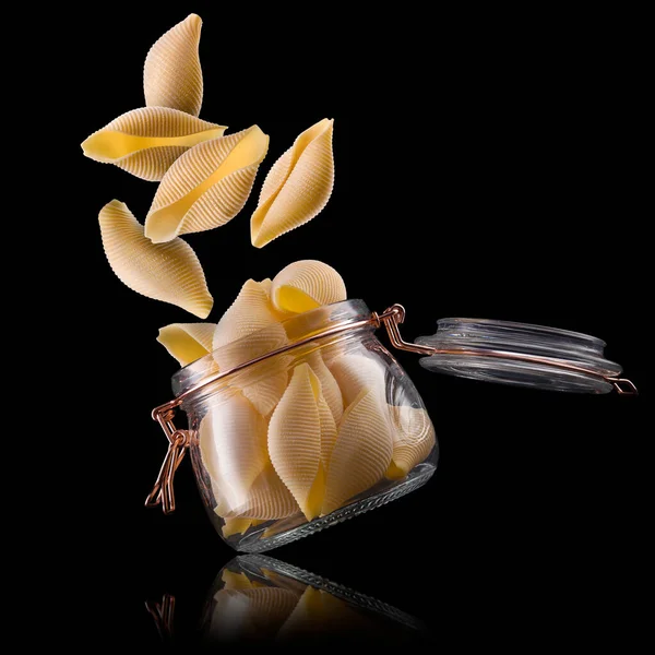 Tarro de conchiglie cáscara de pasta sobre mesa de madera aislada sobre fondo negro —  Fotos de Stock