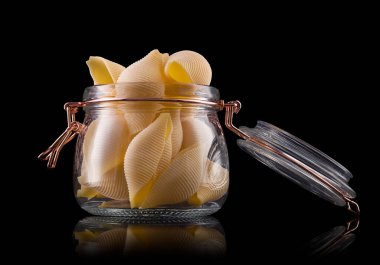 Ahşap masa üzerinde bir kavanoz conchiglie makarna. Siyah arka planda, kırpma yolu ile izole edilmiş. Hamur ürünleri ve hamur işi kavramı