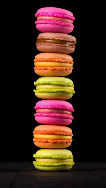 Pilha de macaroons coloridos franceses na mesa de madeira isolada no fundo preto — Fotografia de Stock