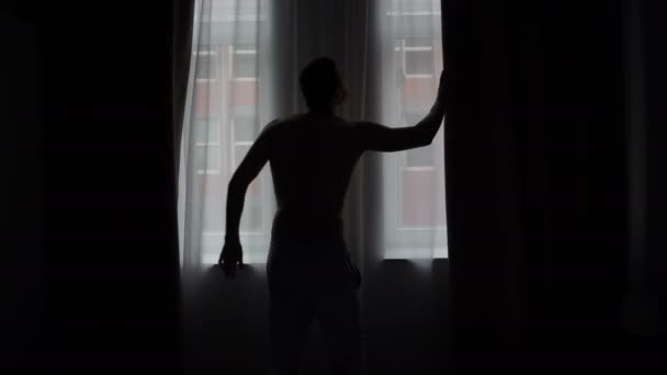 Rideau d'ouverture de silhouette homme, regardant par la fenêtre — Video