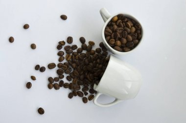 Beyaz arka planda izole edilmiş beyaz seramik fincandan kahve çekirdekleri döküldü.