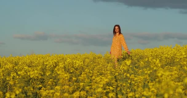 Gyönyörű, sárga ruhás nő sétál át egy sárga mezőn repkéjvirággal. Fiatal, gyönyörű lány, piros ruhában, közel a sárga mező közepéhez, retekvirágokkal..