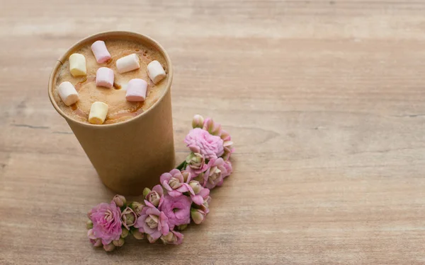 Kâğıt bardakta, ahşap arka planda, pembe çiçekli kahve.