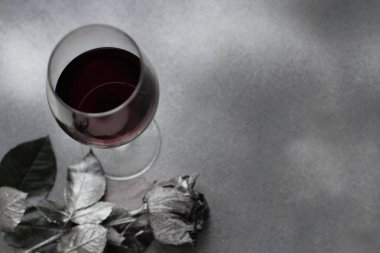 kırmızı şarap cam gümüş Gümüş arka plan üzerinde düz gül ile yatıyordu