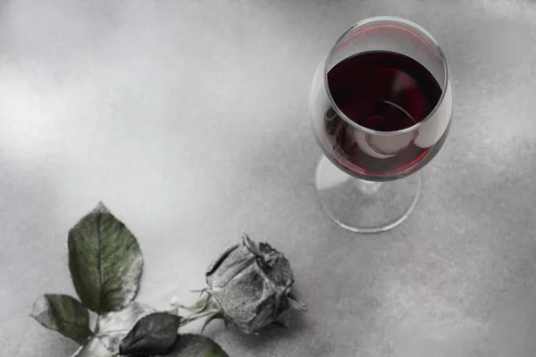 Красное вино в стакане с серебряной розой на серебряном фоне — стоковое фото
