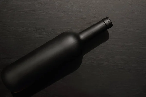 black matte bottle of wine laying on black background, table, top view, copy space