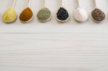 Beyaz ahşap zemin üzerinde tahta kaşıklar içinde farklı baharatlar